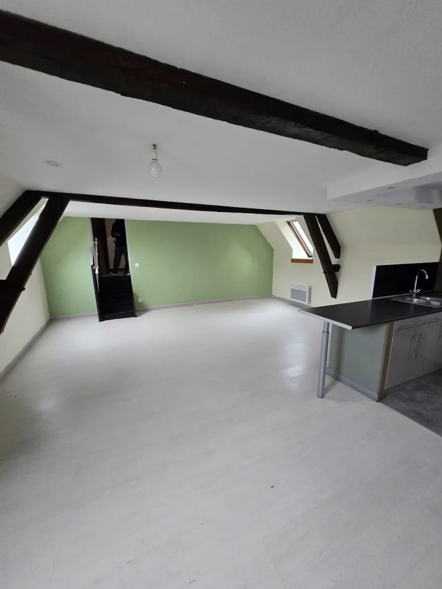 Le Loft des Charpentiers vide : espace ouvert sous charpente, poutres noires, îlot cuisine brut