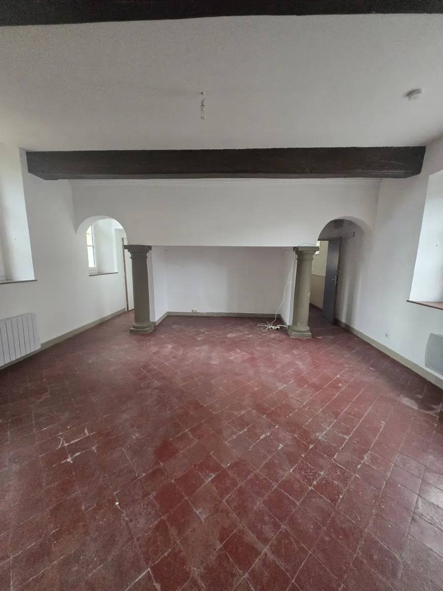 La Salle des Arches vide : colonnes en pierre, arches, carrelage terracotta, murs nus