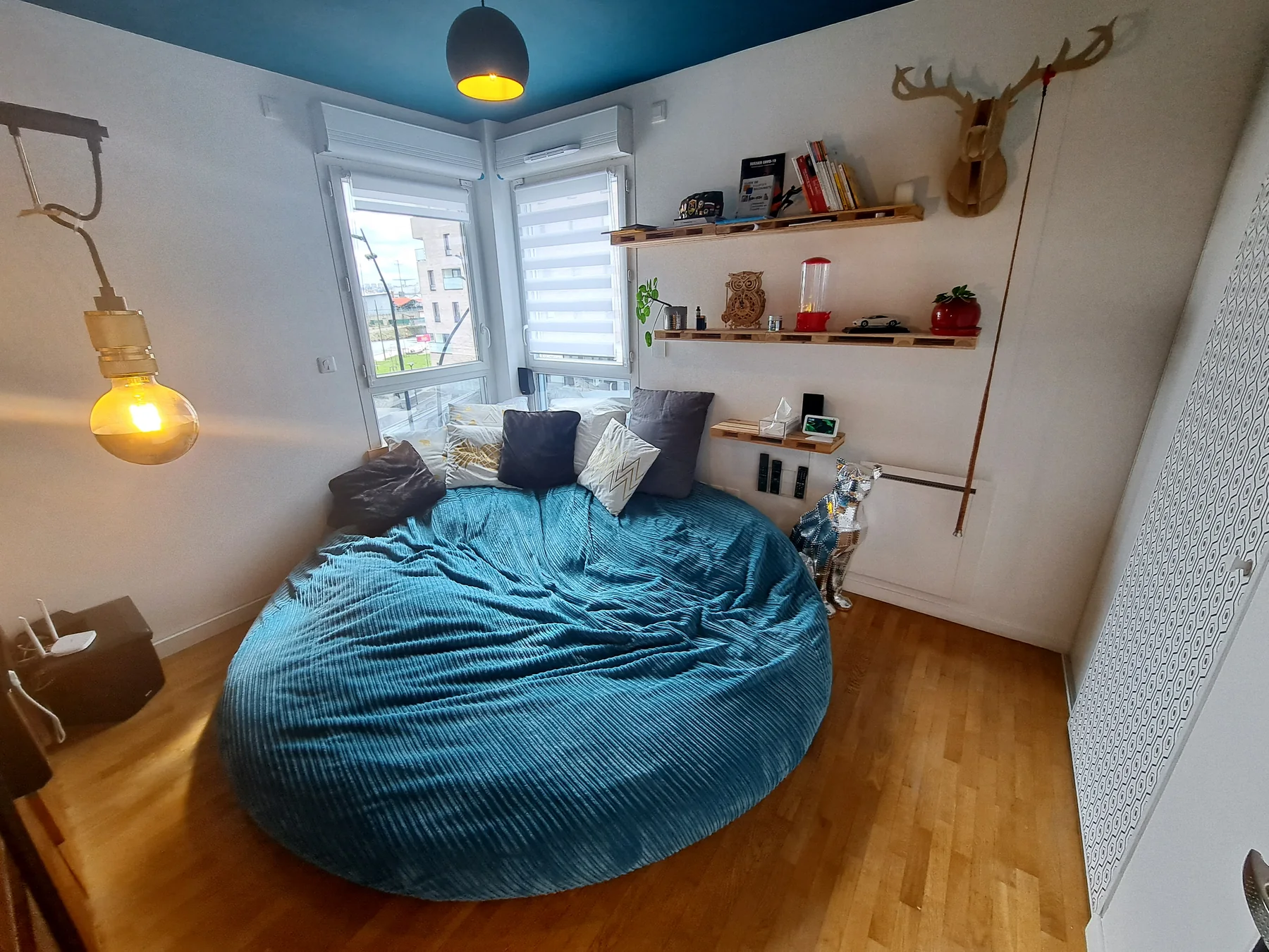 Chambre après rénovation : tête de lit bleu canard, lit double, appliques, décoration murale et atmosphère chaleureuse