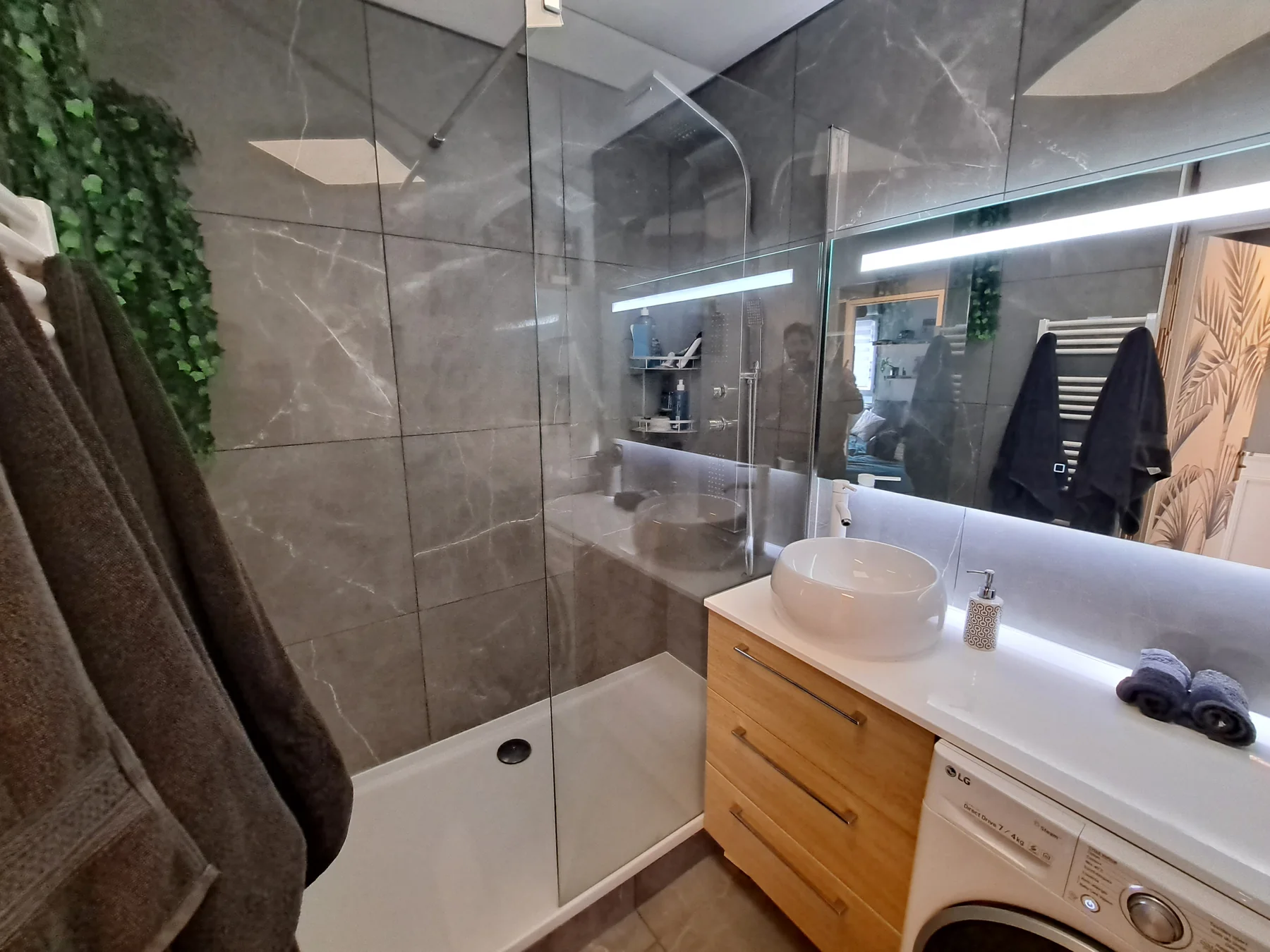 Salle de bain après rénovation : douche, carrelage gris grand format, meuble bois, grand miroir lumineux