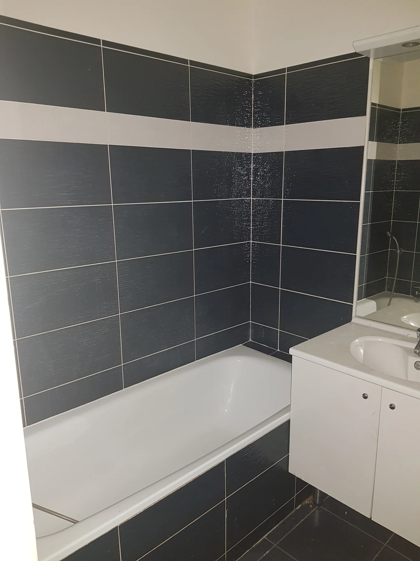 Salle de bain avant rénovation : baignoire, carrelage sombre, meuble blanc simple